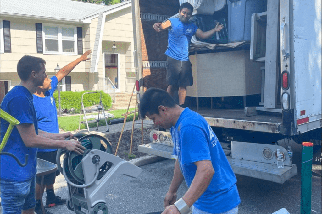 Four amplified moving team members loading furniture from a truck, one directing, another handling a dolly.