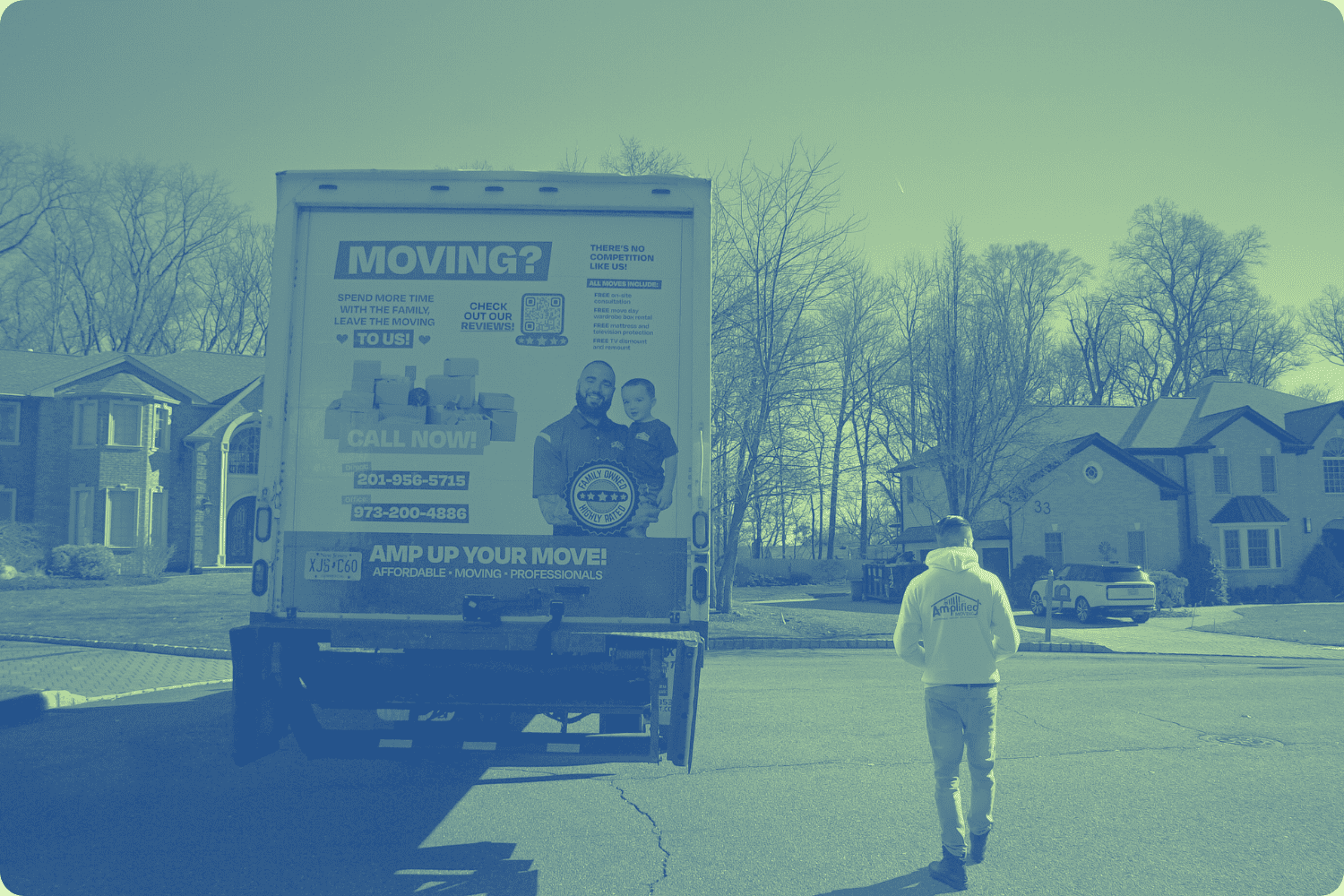 Back view of an amplified moving labeled truck and a man with a yellow amplified moving walking beside it