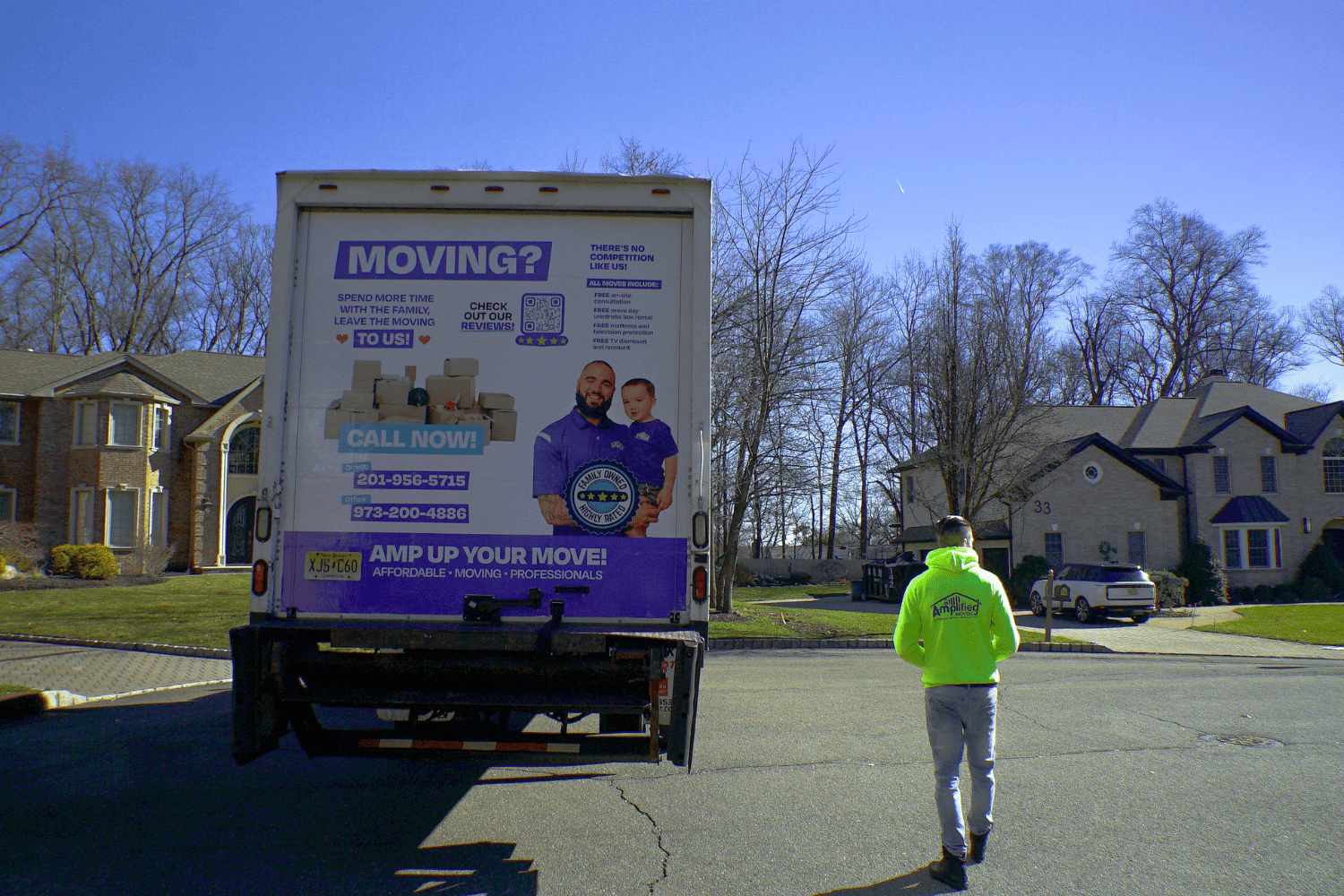 Back view of an amplified moving labeled truck and a man with a yellow amplified moving walking beside it