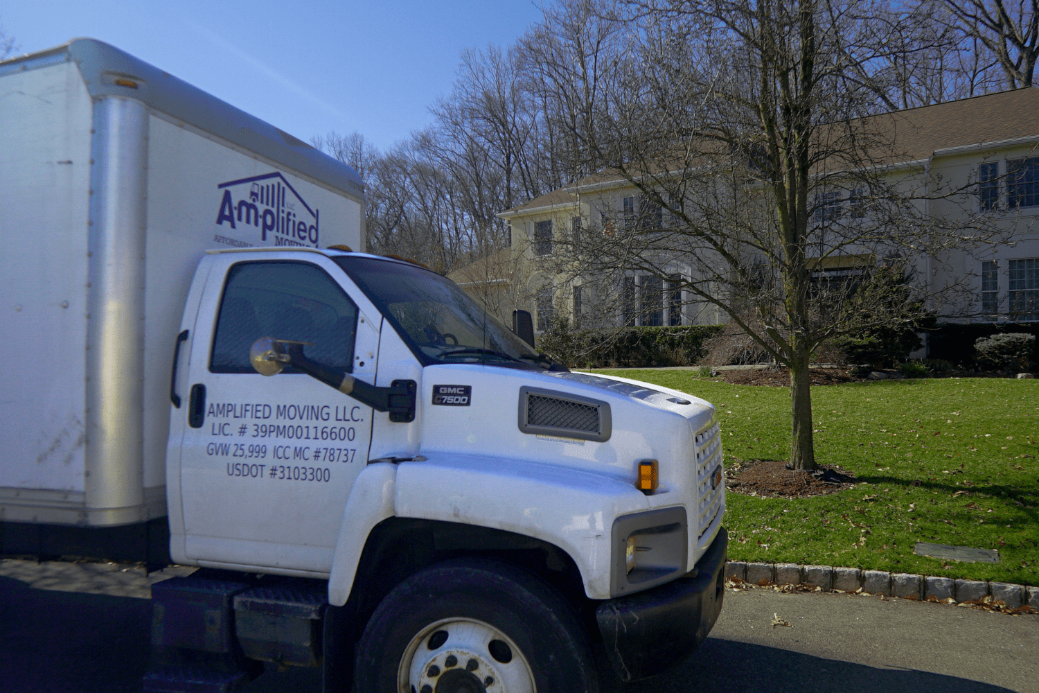 Lateral view of an Amplified moving labeled truck parked in front a large house