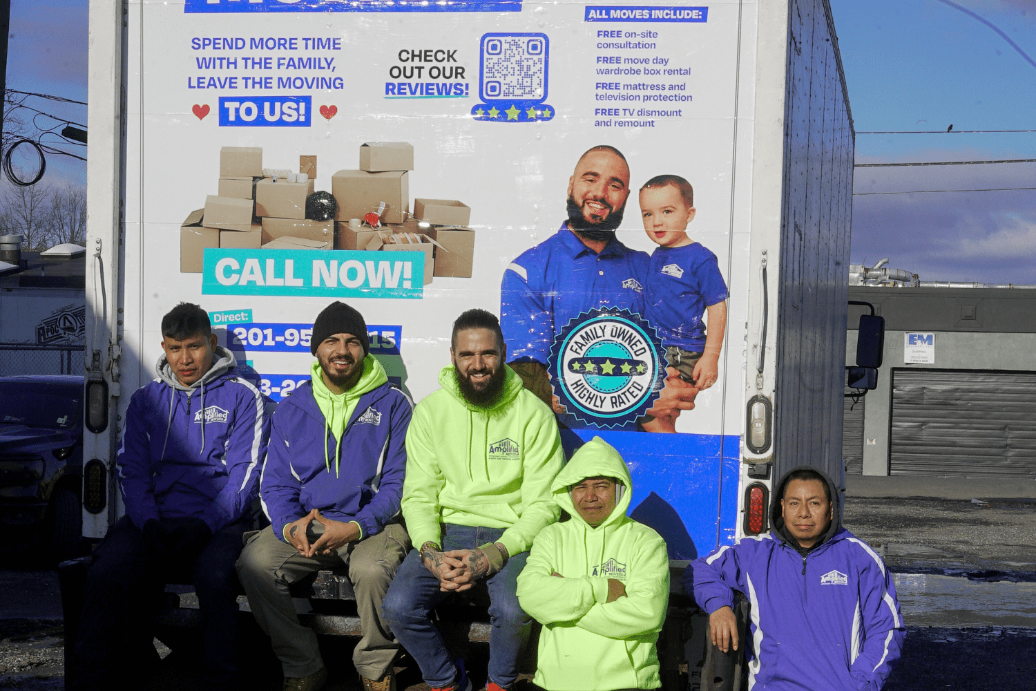 Five team members posing at the back of an amplified moving branded truck