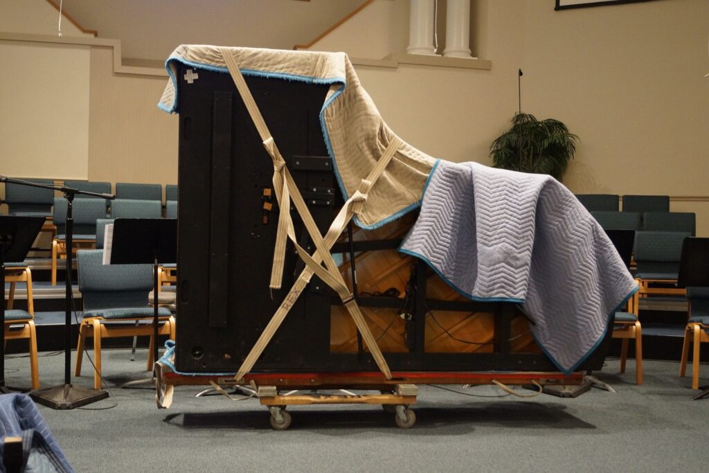 Big piano covered for protection loaded to a dolly ready to be unloaded.