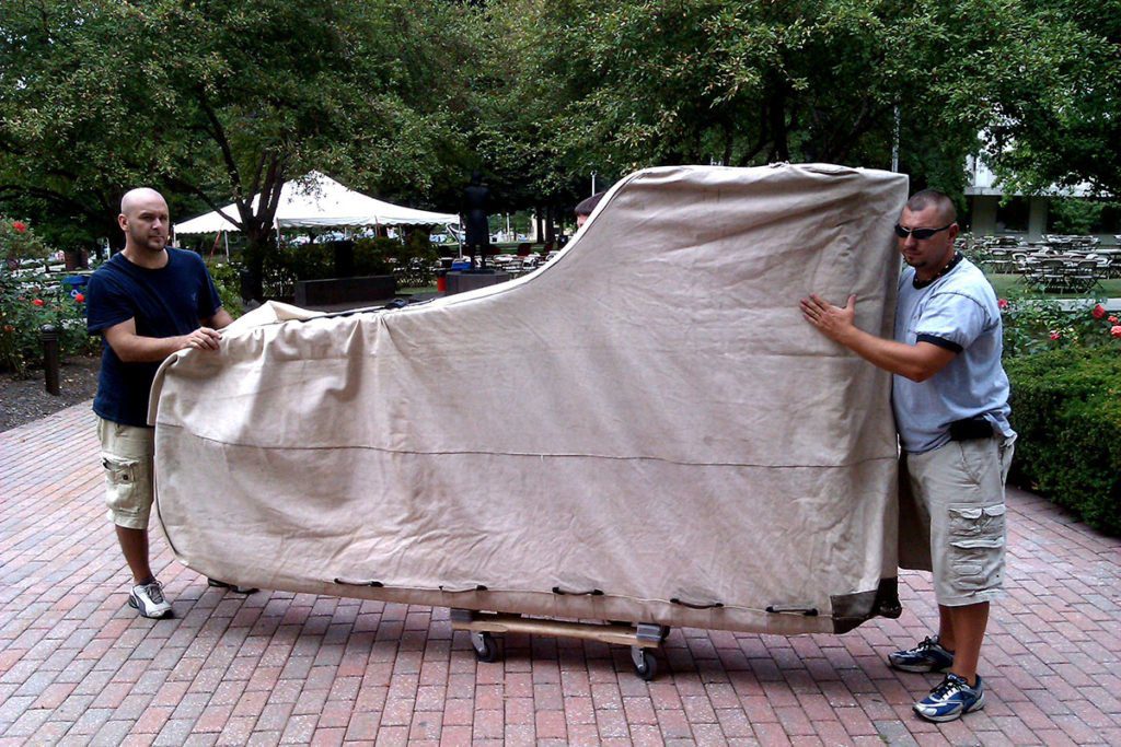 Big piano carefully loaded to a dolly being moved by two men.