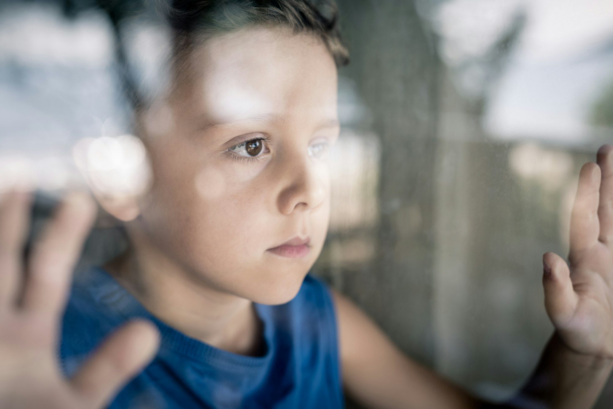 one sad little boy standing near the window at the day time.